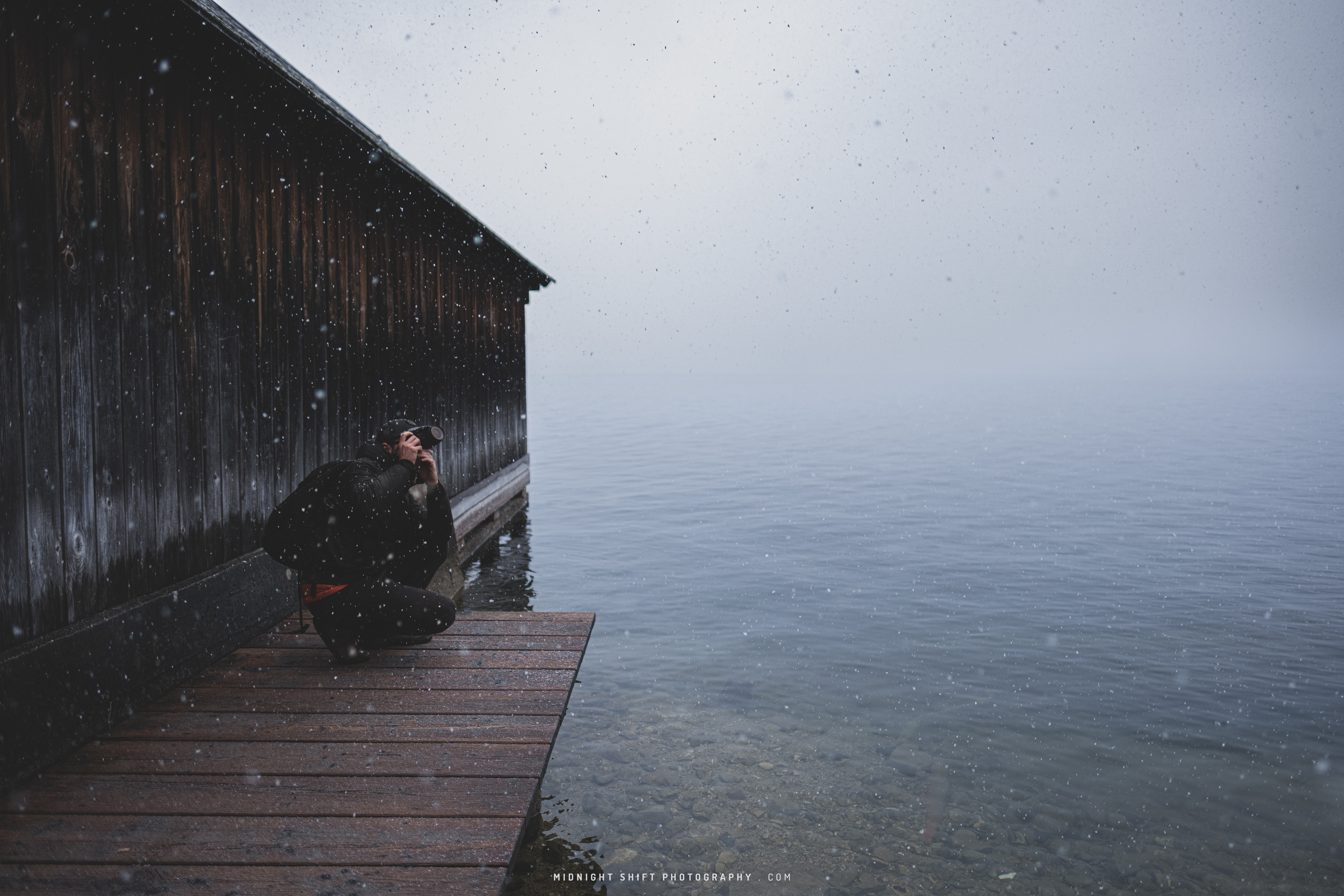 Filipe, crouching like a tiger, on a pier at the edge of the lake, photographing the mountains surrounding Hallstatt Lake.